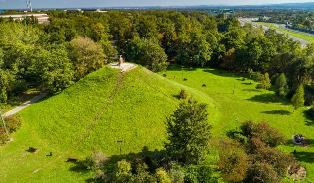 Usypany z ziemi duży kopiec, porośnięty trawą. Na szczycie pomnik.